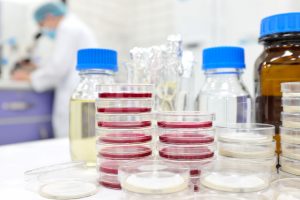 photo with objects showcasing body fluid samples in the foreground and a scientist looking into the microscope in the background