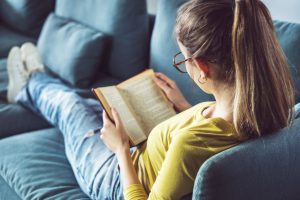 A young woman is sitting on a couch and reading a book